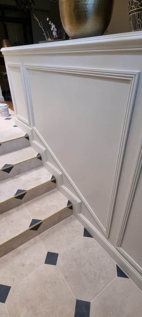 Soubassements moulurés blancs suivant la pente de l'escalier, carrelage cabochons et nez de marche en laiton