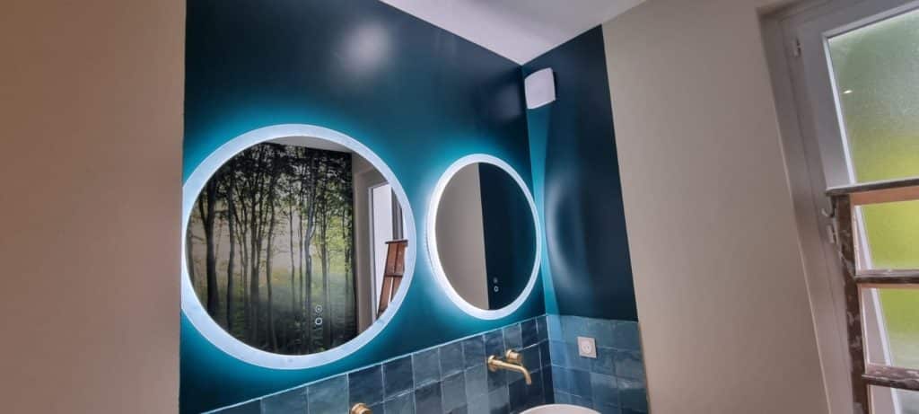 Salle de bain bleu canard avec crédence en zellige, miroirs LED rétroéclairés, robinetterie murale dorée et vasque à poser