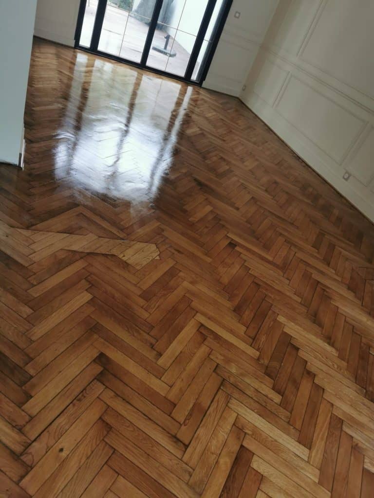 Parquet point de Hongrie fraîchement vitrifié avec finition brillante, baies vitrées noires et moulures blanches