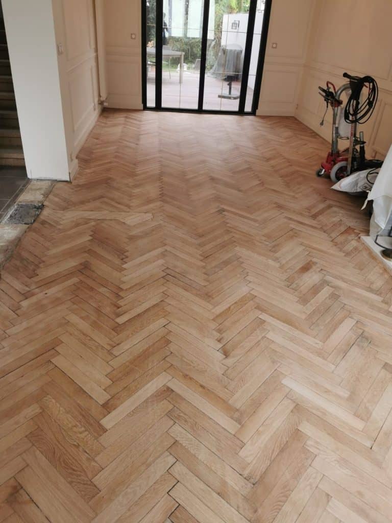 Parquet point de Hongrie après ponçage, bois brut prêt pour vitrification, baies vitrées en arrière-plan