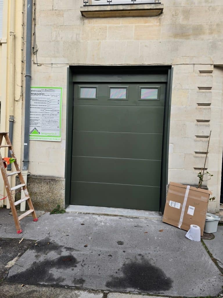Porte de garage sectionnelle vert bronze avec hublots, posée sur façade en pierre de Bordeaux