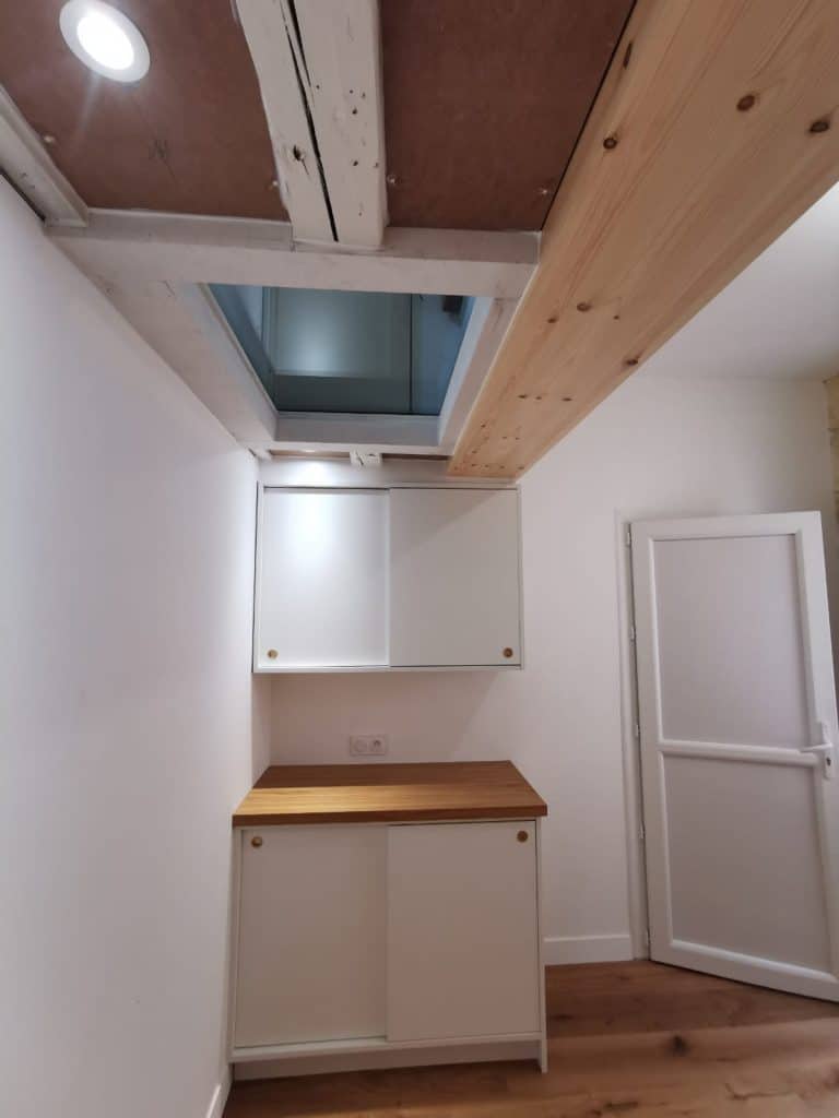 Cuisine rénovée dans une échoppe bordelaise avec poutres apparentes, velux, meubles blancs, plan bois et poignées dorées